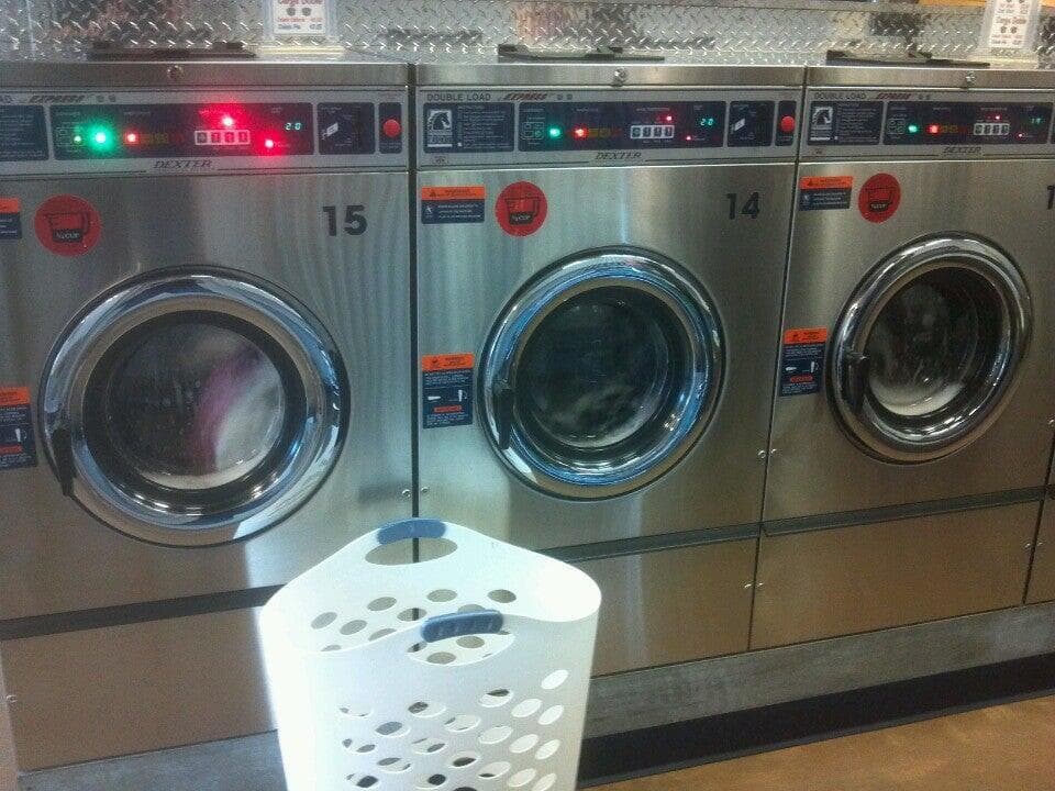 Three stainless-steel Dexter front-load washers numbered 14 and 15 with a white laundry basket in front